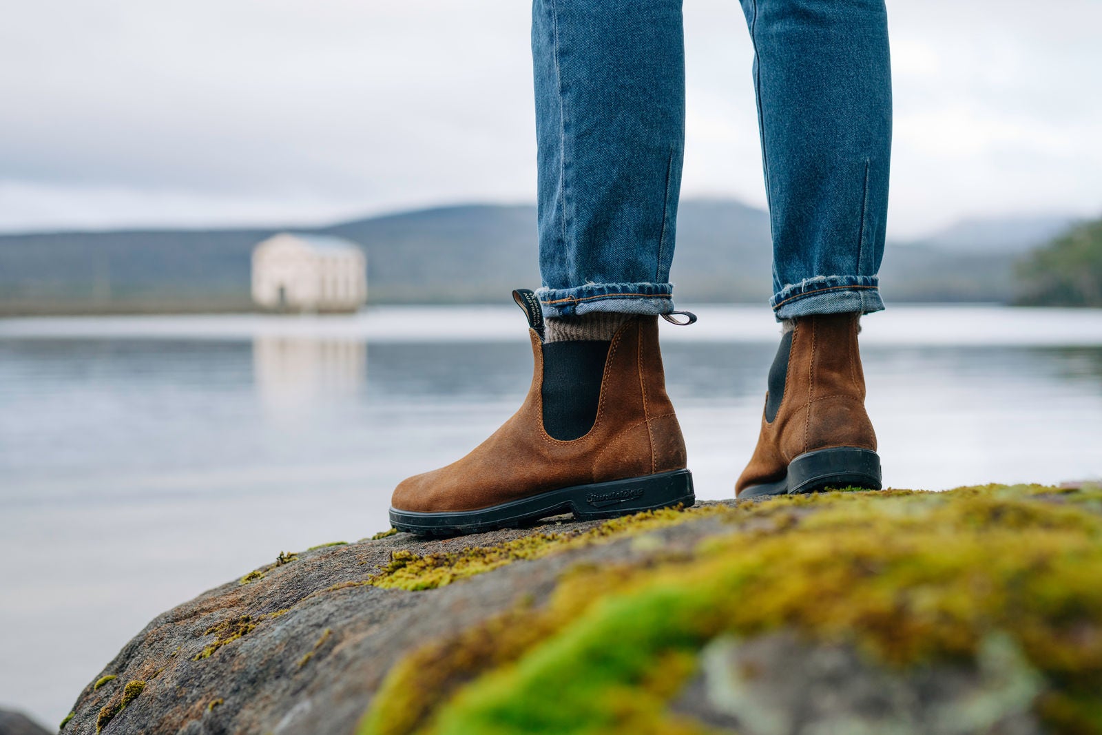 person wearing blundstone boots while standing on rock overlooking a water lake view